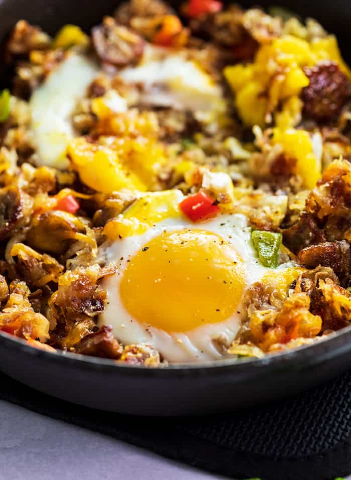 This breakfast skillet is loaded with crispy golden hash, mouth-watering sausage, and perfectly cooked eggs. All you need is a single skillet to make this deliciously satisfying breakfast! | The Cozy Cook | #eggs #hash A close up shot of a baked egg in an iron skillet with hash, sausage, and bell peppers