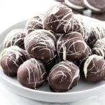 A white dessert stand with a stack of Oreo Truffles on top and Oreo Cookies in the background.
