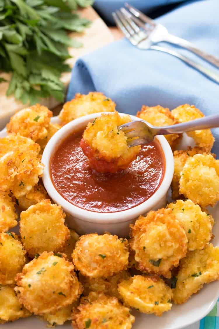 Cheese-filled tortellini that’s surrounded by a crispy Parmesan crust, fried to golden perfection and dipped in warm marinara sauce. a fork dipping a fried and breaded tortellini bite into marinara sauce