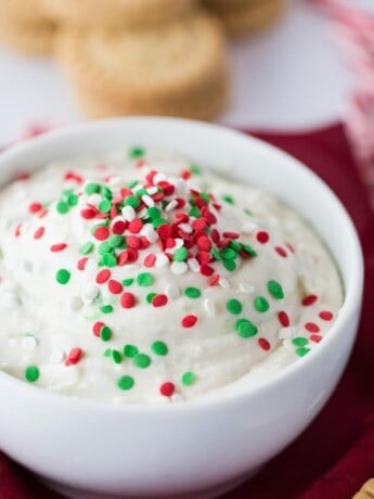 A white bowl of Christmas cookie dip with red and green sprinkles on top.