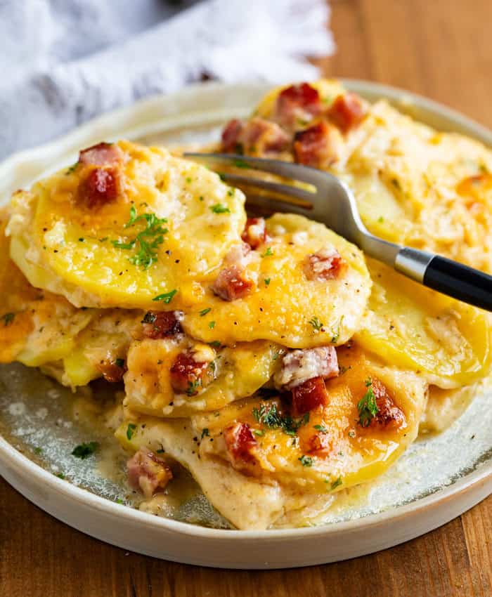 A plate full of cheesy scalloped potatoes with ham with a fork in the background.