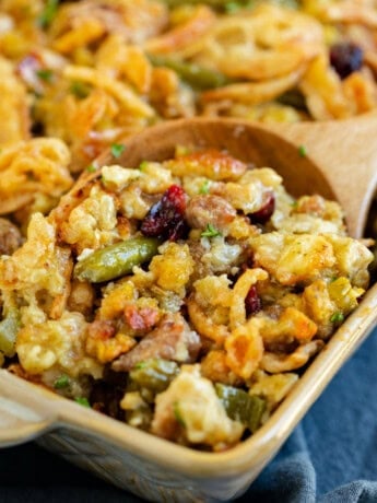 A casserole dish with a wooden spoon scooping out stuffing casserole with green beans.
