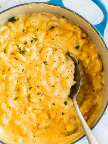 A spoon scooping up creamy Mac and Cheese from a Dutch oven.