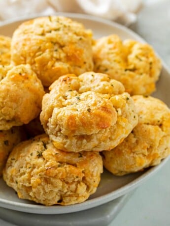 A white plate with a pile of Cheddar Bay Biscuits with parsley on top.