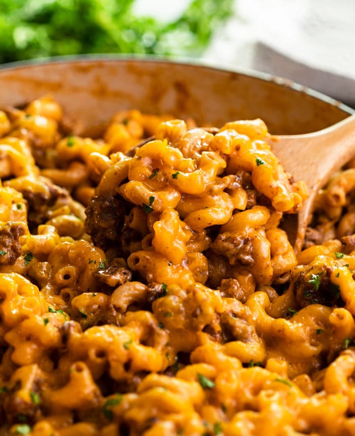 A skillet with a wooden spoon scooping up Cheeseburger Casserole
