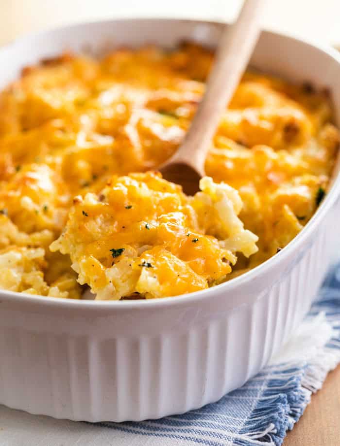 A wooden spoon laying across a white casserole dish filled with cracker barrel hashbrown casserole.