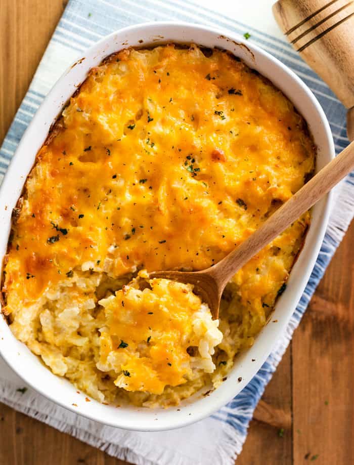 Overhead view of a wooden spoon laying in a white casserole dish that's full of hashbrown casserole.