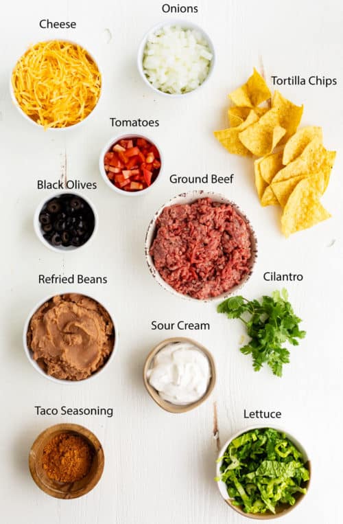 This Taco Casserole is easy to make ahead of time and bake later! It's loaded with juicy ground beef and your favorite Mexican toppings for a perfect weeknight dinner! #doritos #fritos #recipe #mexicanrecipes #easydinnerideas #familydinner #groundbeefrecipes Overhead view of ingredients needed to make taco casserole on a white surface.