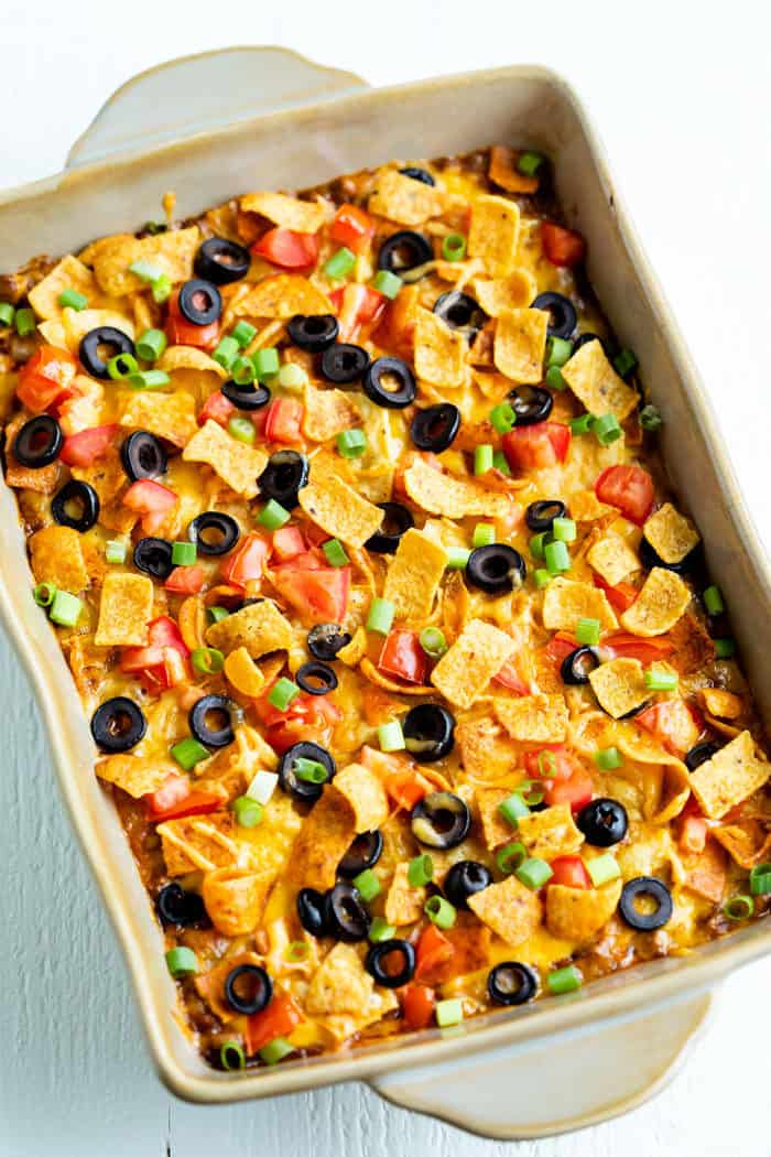 This Taco Casserole is easy to make ahead of time and bake later! It's loaded with juicy ground beef and your favorite Mexican toppings for a perfect weeknight dinner! #doritos #fritos #recipe #mexicanrecipes #easydinnerideas #familydinner #groundbeefrecipes Overhead view of Taco Casserole in a casserole dish topped with fritos, tomatoes, and black olives.
