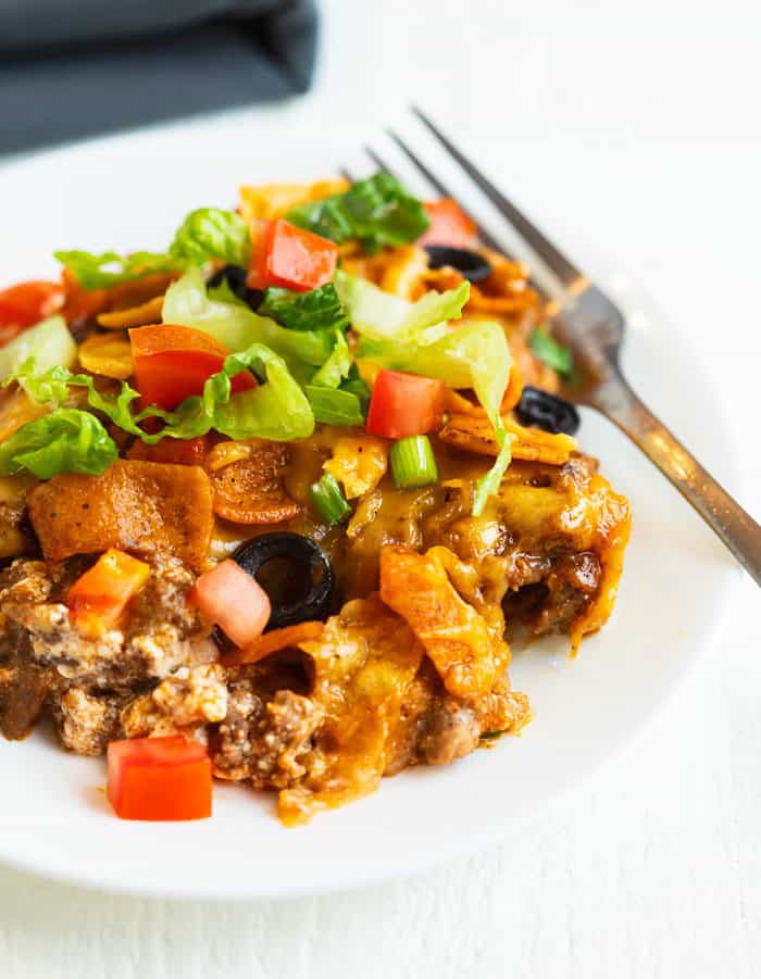 Taco Casserole on a white plate, topped with shredded lettuce and diced tomatoes.