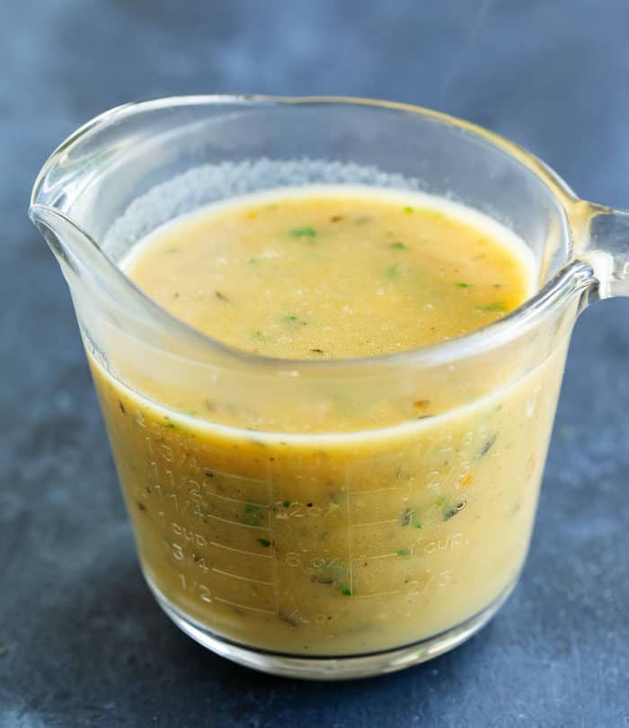 A class measuring cup filled with homemade chicken gravy on a blue surface.