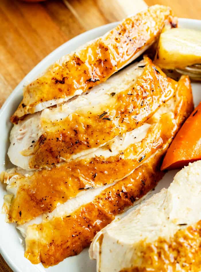 Thick slices of roasted chicken with crispy skins on a white plate.
