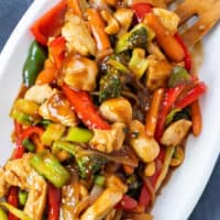 A white platter with chicken stir fry in a brown stir fry sauce.