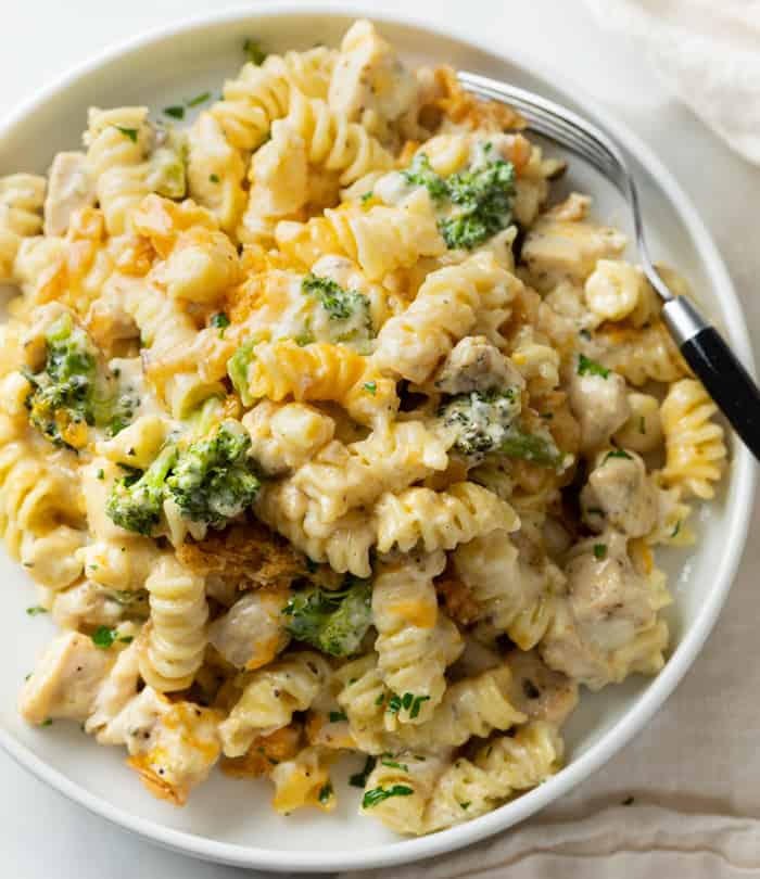 A white plate with Chicken Noodle Casserole with with a creamy mushroom cheese sauce and broccoli.