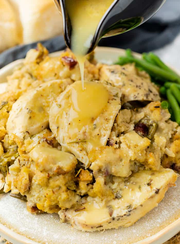 A plate with chicken and stuffing with gravy being drizzled on top and green beans in the background.