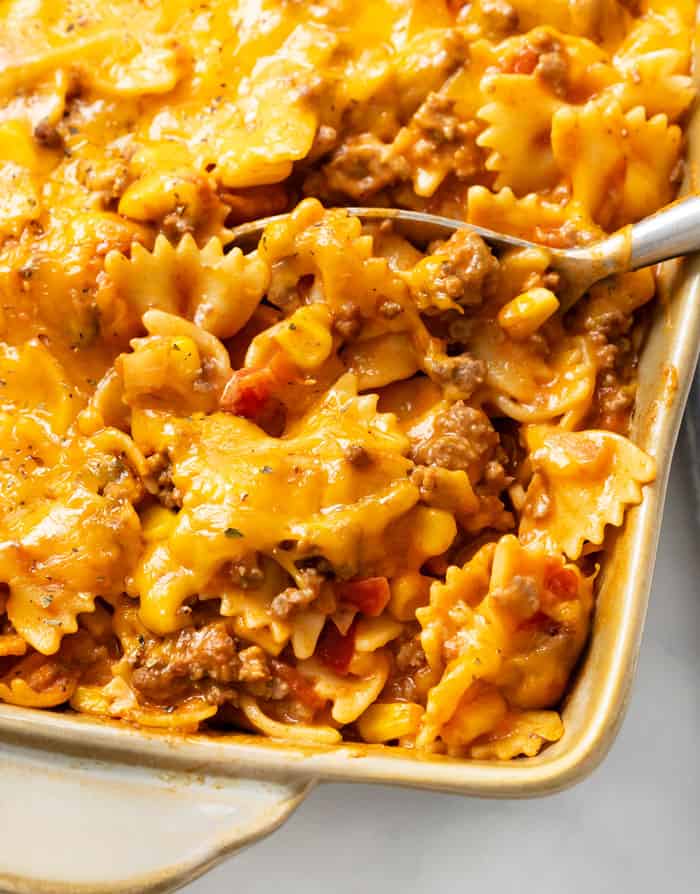 A spoon full of sloppy joe casserole in a casserole dish.