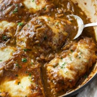 A spoon scooping up French Onion Chicken topped with melted cheese and caramelized onions.