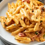 Creamy Buffalo Chicken Pasta on a white plate with chicken and diced tomatoes.