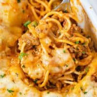 A spoon holding up baked spaghetti from a casserole dish.