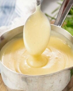 A spoon pulling up thick and smooth cream of chicken soup from a saucepan.