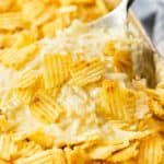 A spoon scooping up creamy funeral potatoes with crushed potato chips on top.