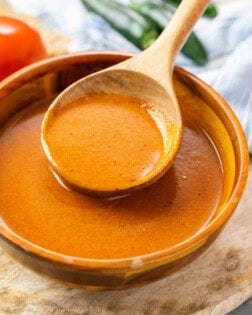 A bowl with a wooden spoon filled with homemade enchilada sauce.