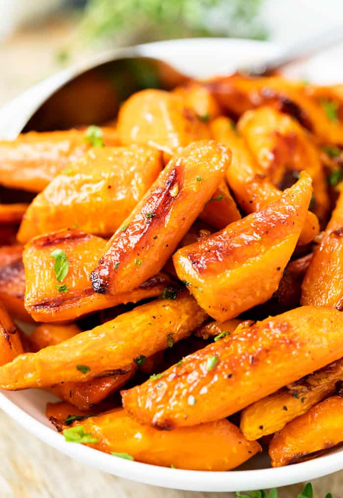 Roasted carrots in a white bowl with a spoon in the background.