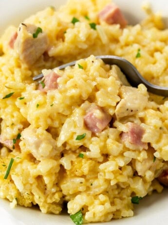 A white plate with a fork scooping up Chicken Cordon Bleu Casserole with ham, chicken, and rice.