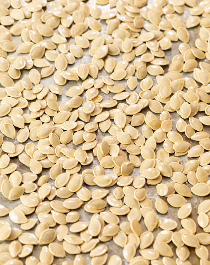 Raw pumpkin seeds on a light baking sheet before being roasted.