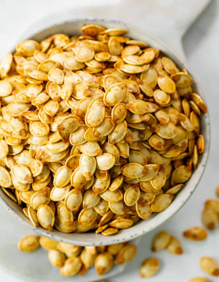 A white bowl overflowing with crispy roasted pumpkin seeds.