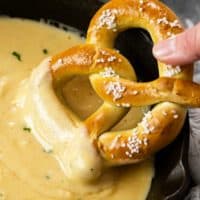 A hand dipping a soft pretzel into a skillet of Beer Cheese Dip.