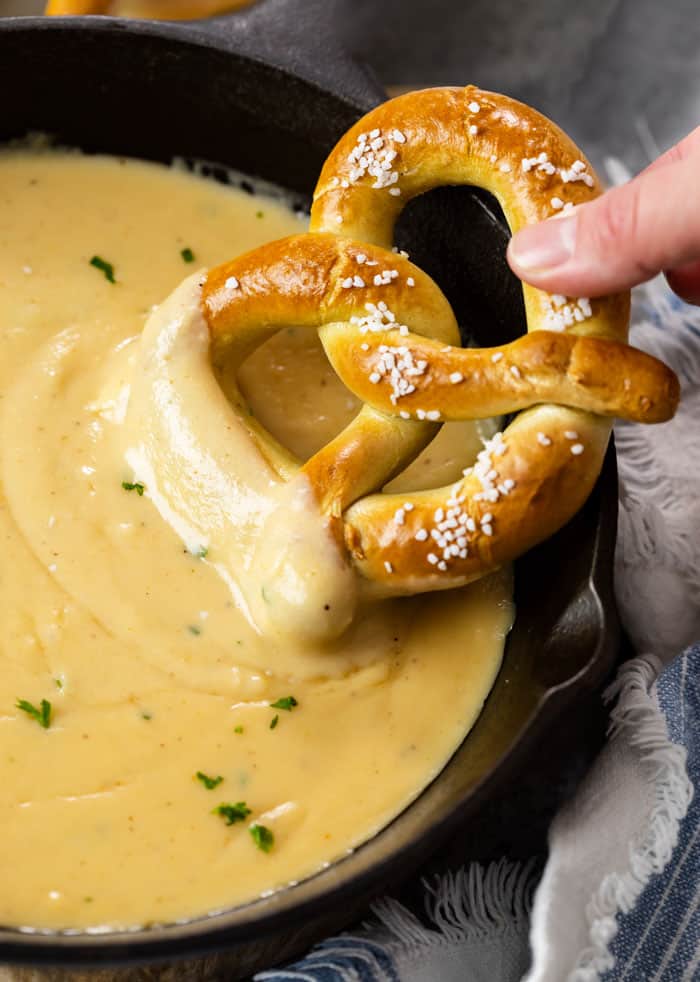 A cast iron skillet with beer cheese dip with a soft pretzel being dipped in it.