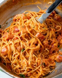 A skillet with creamy tomato pasta with kitchen tongs.