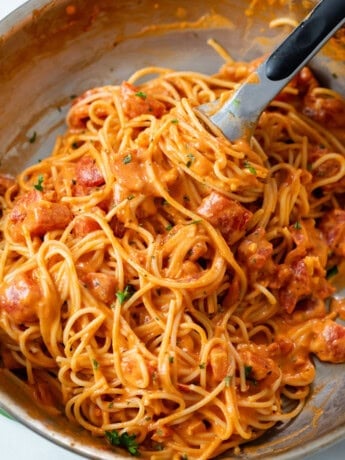 A skillet with creamy tomato pasta with kitchen tongs.
