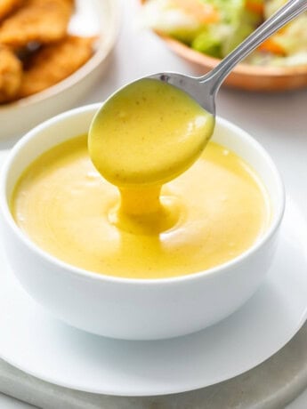 Honey Mustard in a white bowl with a spoon pouring it out.