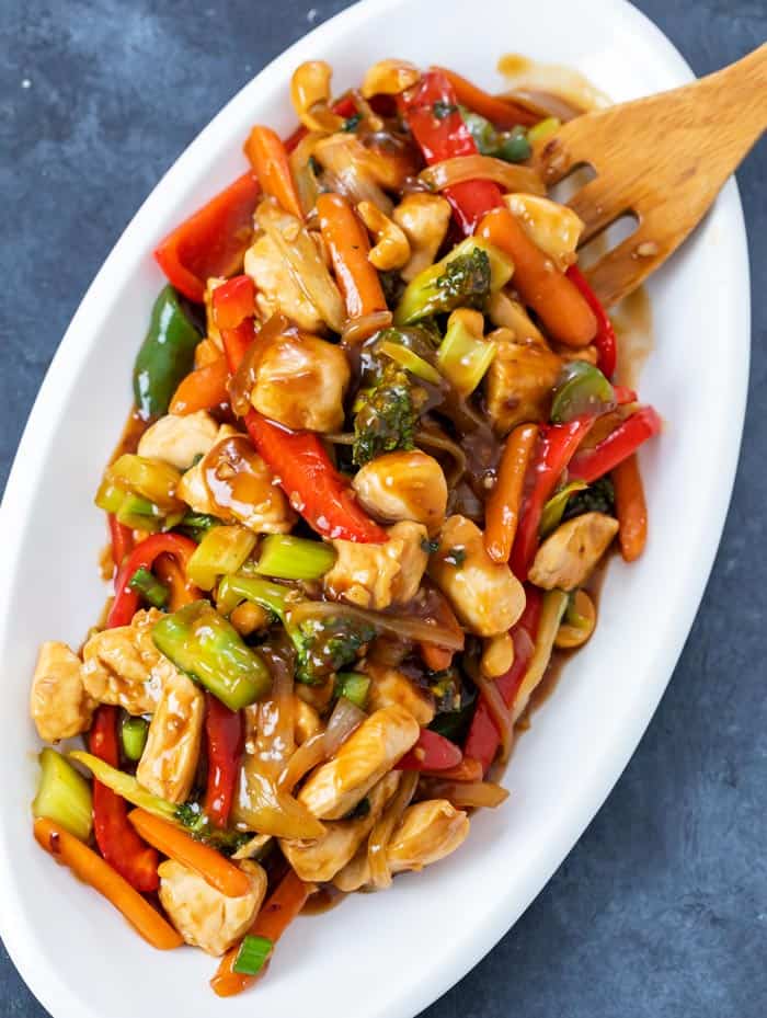 Overhead view of a white platter with chicken stir fry covered in sauce.