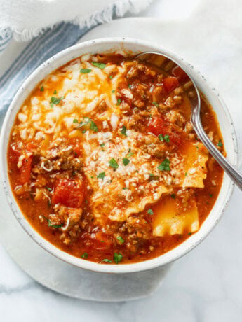 Lasagna Soup in a white bowl with cheese on top and a spoon on the side.