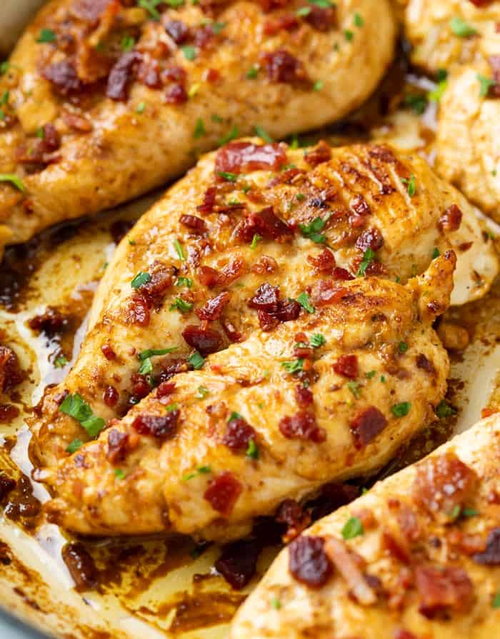A skillet with marinated chicken topped with bacon and parsley.