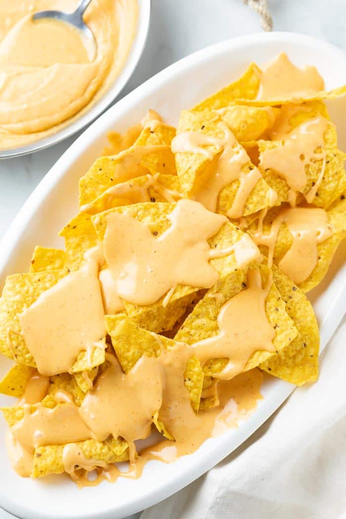 A white platter with tortilla chips topped with Nacho Cheese Sauce.
