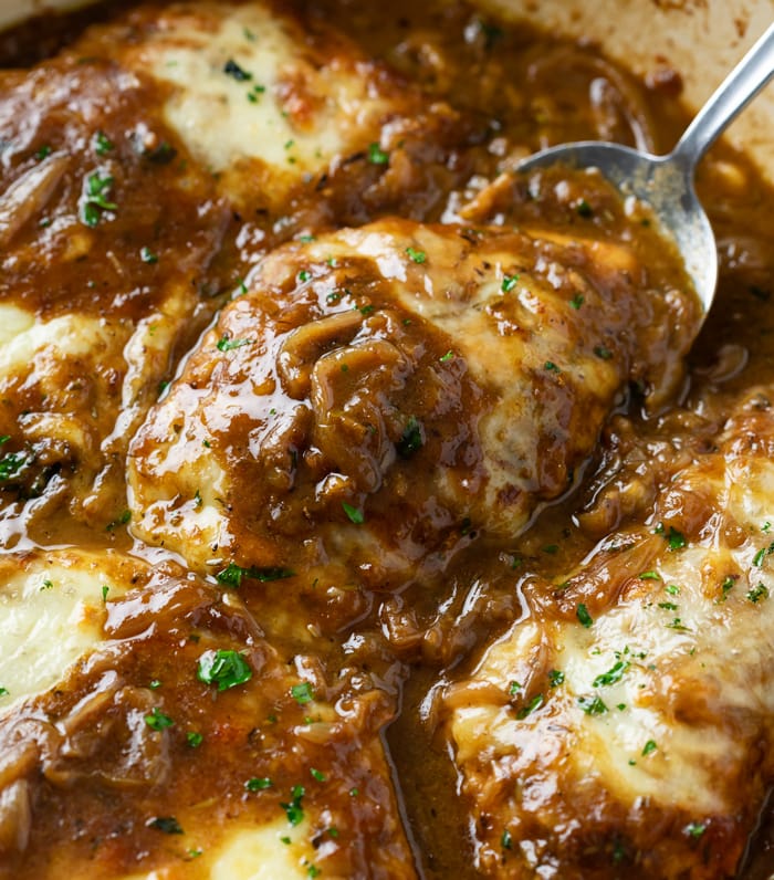 A spoon scooping up French Onion Chicken from a skillet with melted cheese on top.