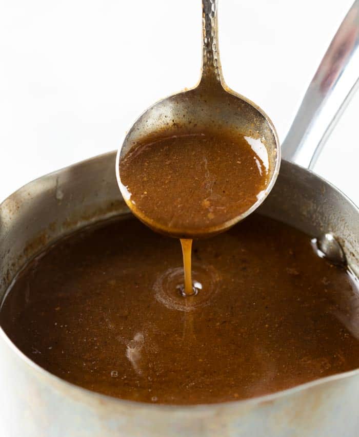 A saucepan filled with brown pot roast gravy with a ladle spooning it out.