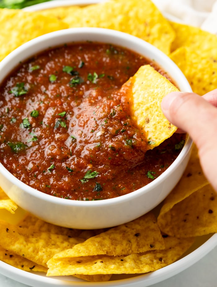 A white bow full of salsa with a tortilla chip being dipped into it.