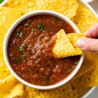 A white bowl of Homemade Salad with a tortilla chip being dipped into it.