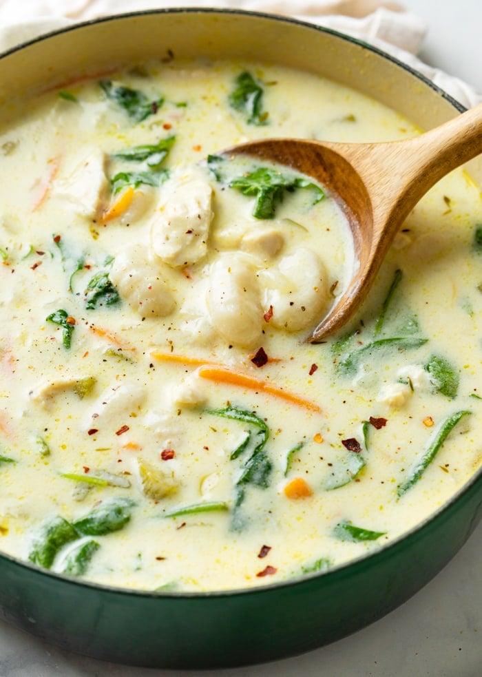 A wooden spoon scooping up Chicken Gnocchi Soup from a pot.