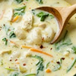 A soup pot full of Chicken Gnocchi Soup with a Wooden Spoon scooping it up.