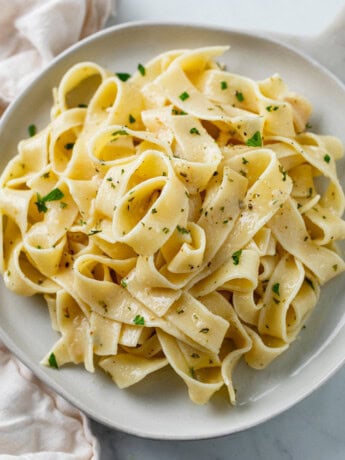 A white plate with buttered noodles topped with herbs.