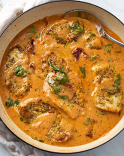 A skillet filled with Tuscan Chicken in sauce with sundried tomatoes and spinach.