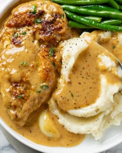 A white Plate with creamy garlic chicken next to mashed potatoes and green beans.