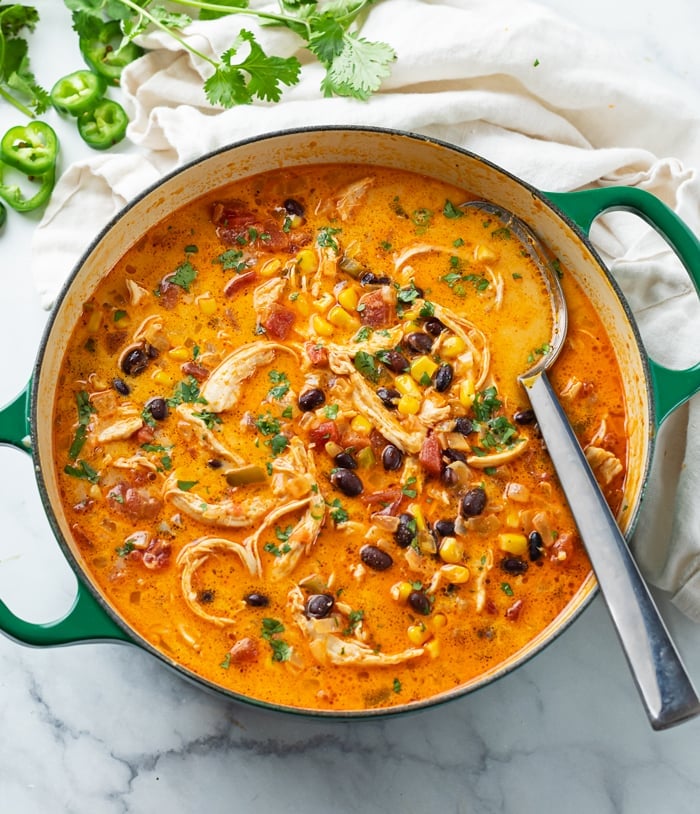 A soup pot with Chicken Enchilada Soup and a spoon in it with cilantro on the side.