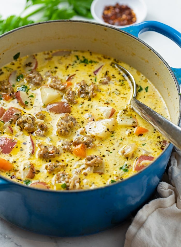 A blue soup pot filled with sausage potato soup with a spoon in it.